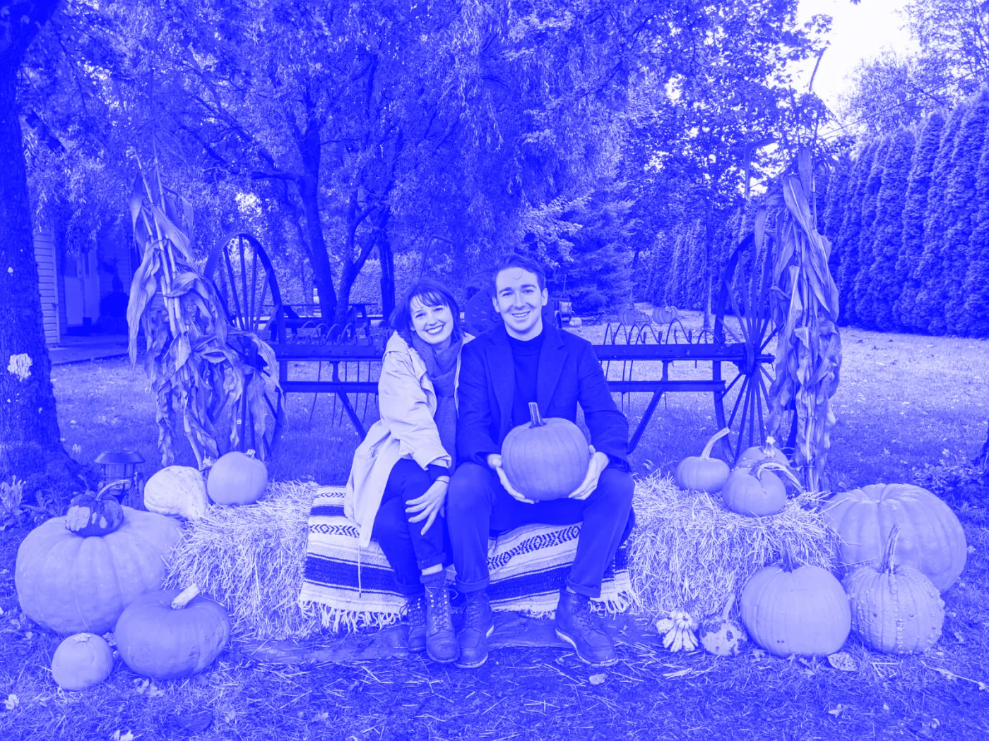 Jess and Patrick on a haybail surrounded by pumpkins. Patrick is holding a pumpkin.